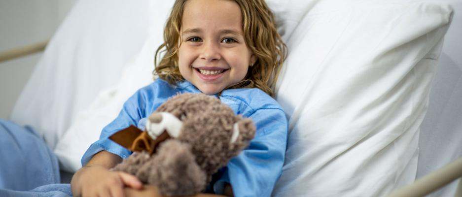 Child in hospital bed holding teddy bear