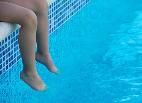 A white person's legs hanging off the side of a pool with the toes in the water
