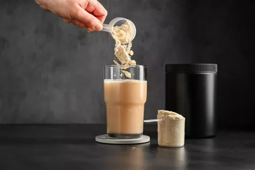 A hand pouring protein powder into a drink