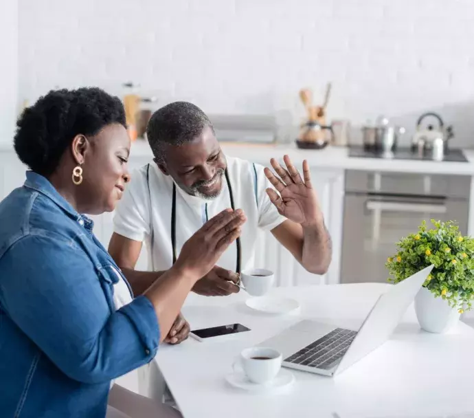 A black couple smiling and working on a laptop in the kitchen