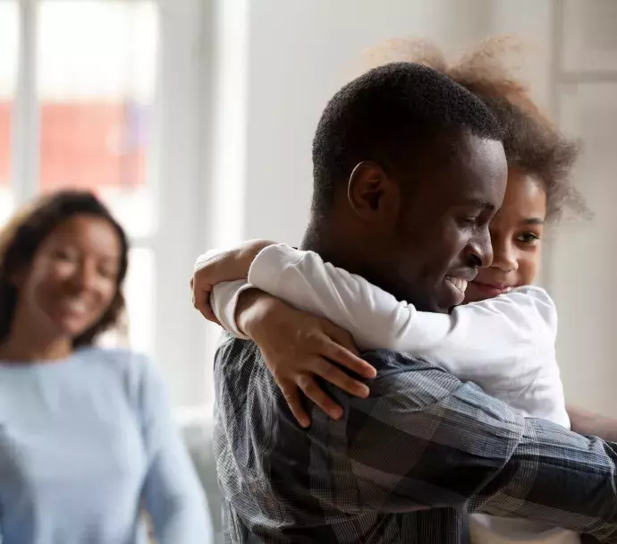 Dad hugging young daughter with mom smiling