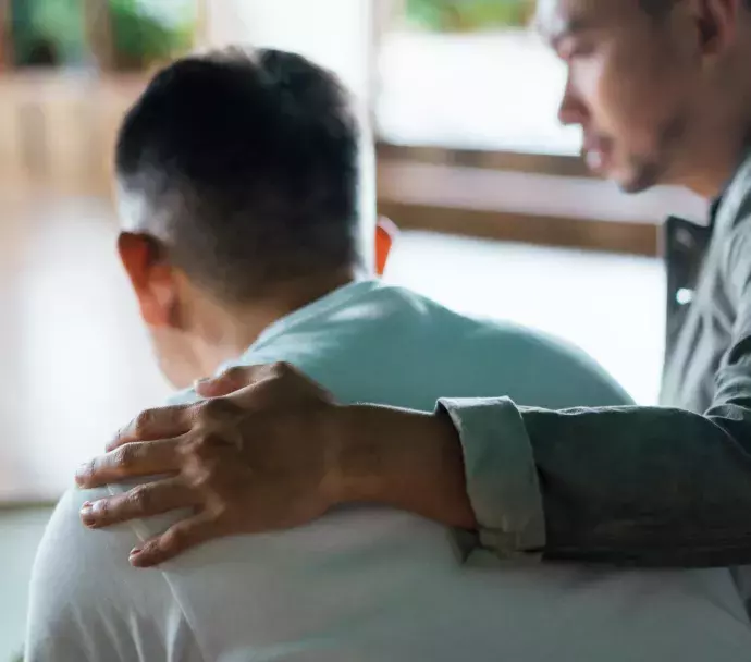 Person with their arm around the shoulder consoling another person