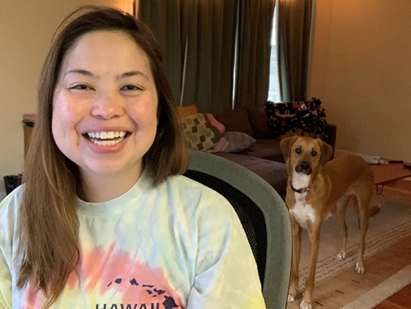 smiling woman sitting in chair wearing tie dye shirt with dog in background